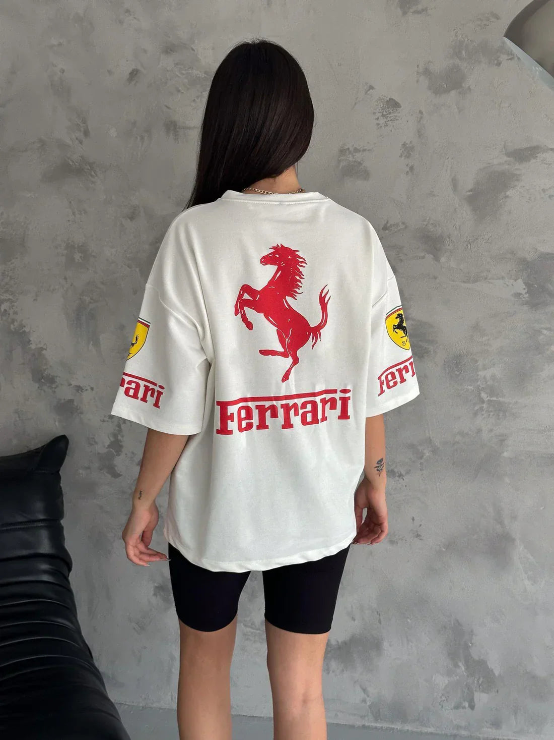 Person wearing a Ferrari logo t-shirt against a gray wall