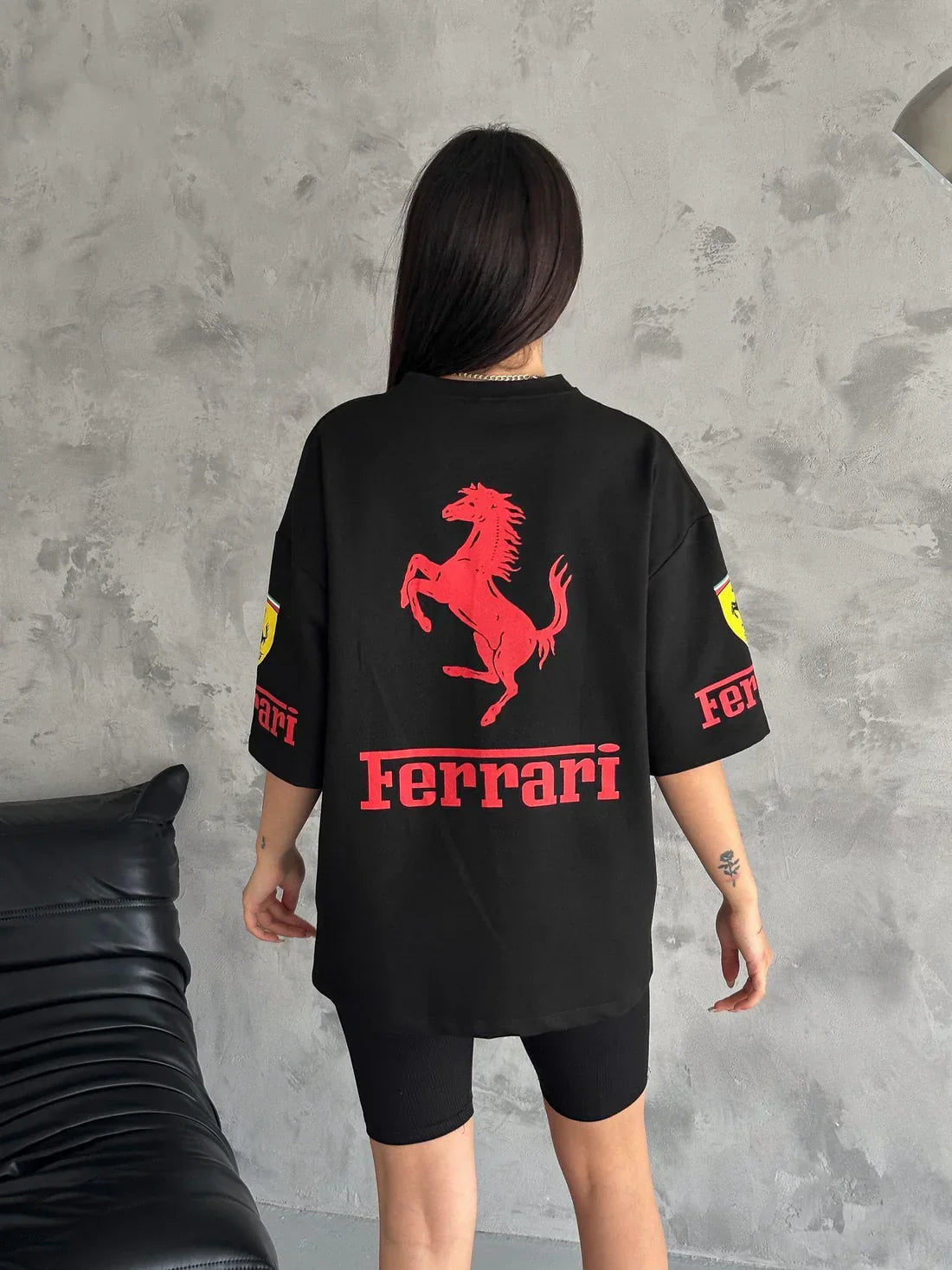 Person wearing a black Ferrari t-shirt with red logo against a gray wall.