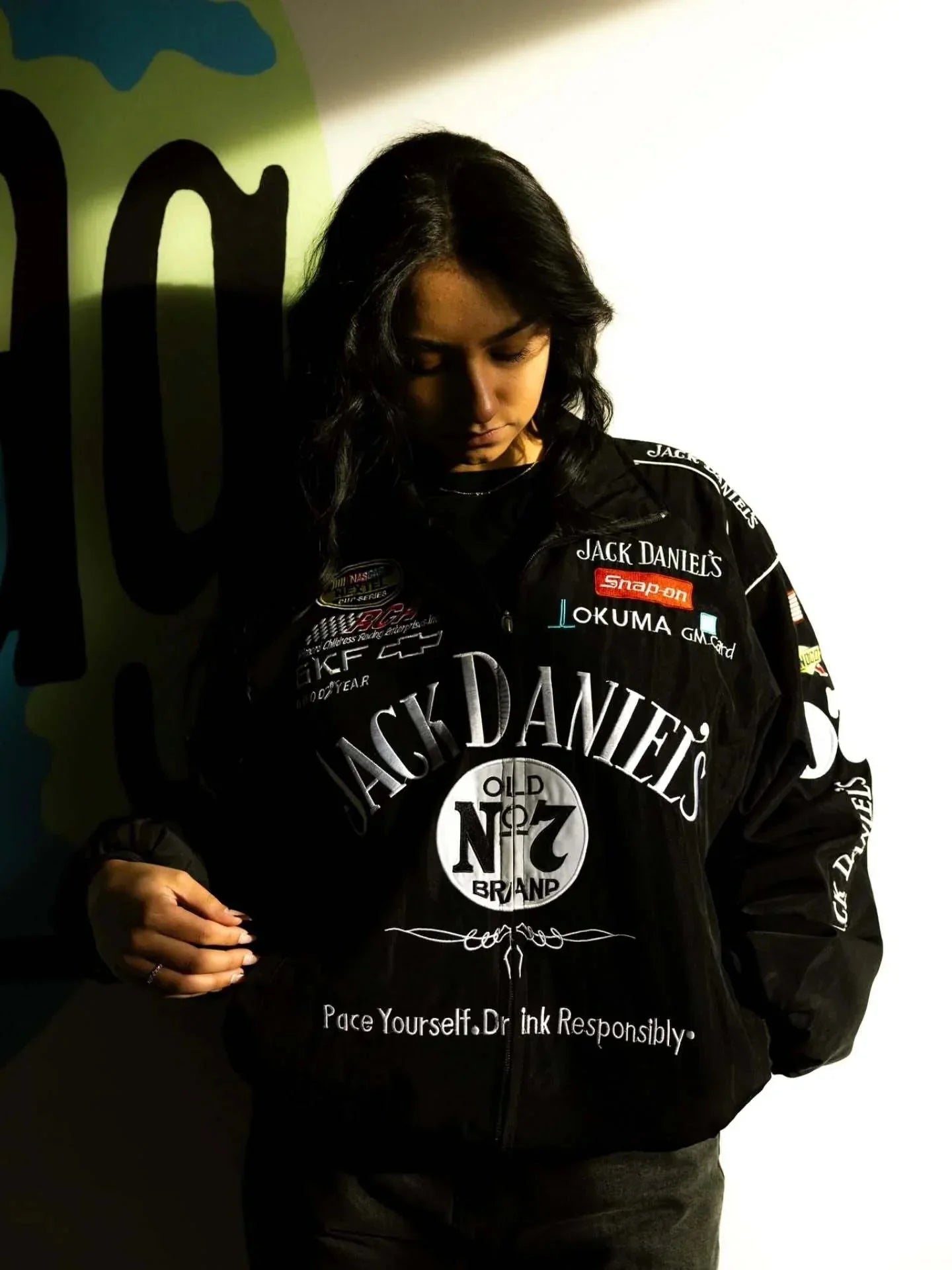 Person wearing a black sweatshirt with multiple brand logos against a dark background