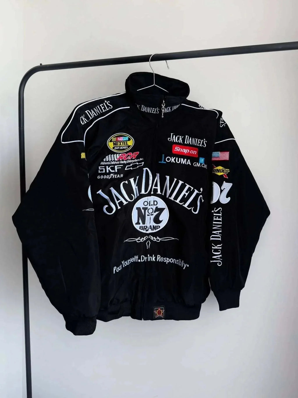 Black jacket with multiple brand logos on a hanger against a white background