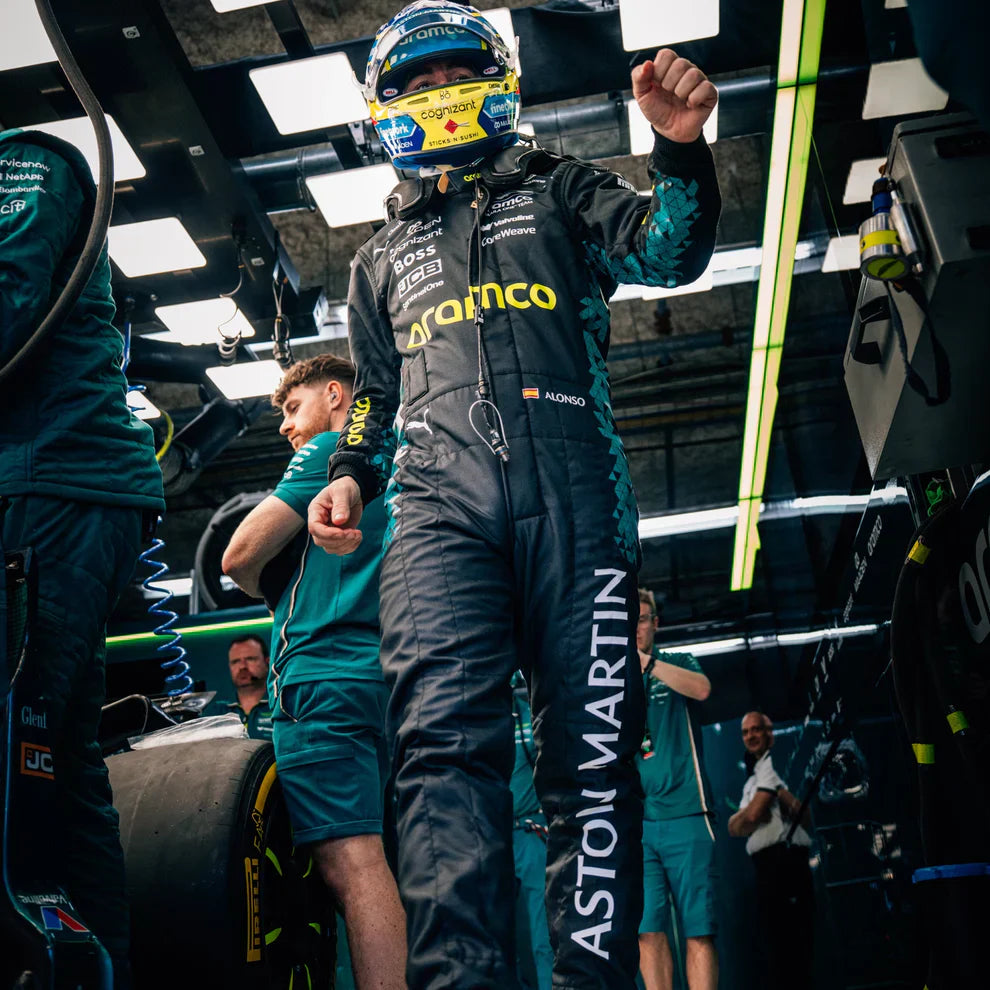 Person in racing suit and helmet in a garage with 'Aston Martin' branding