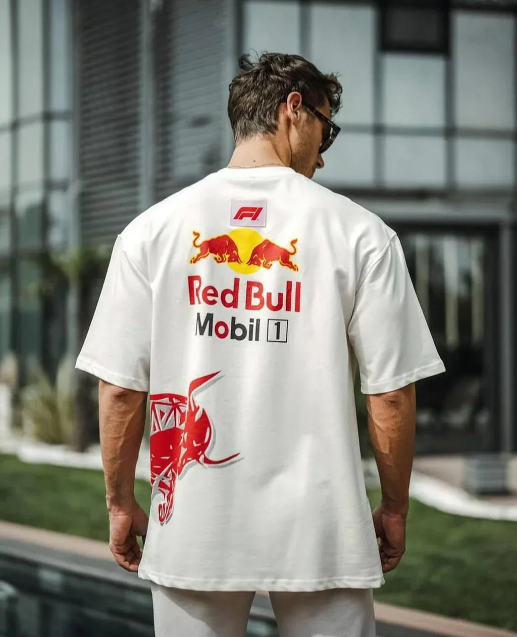 Man wearing a white t-shirt with Red Bull and Mobil 1 logos outdoors.
