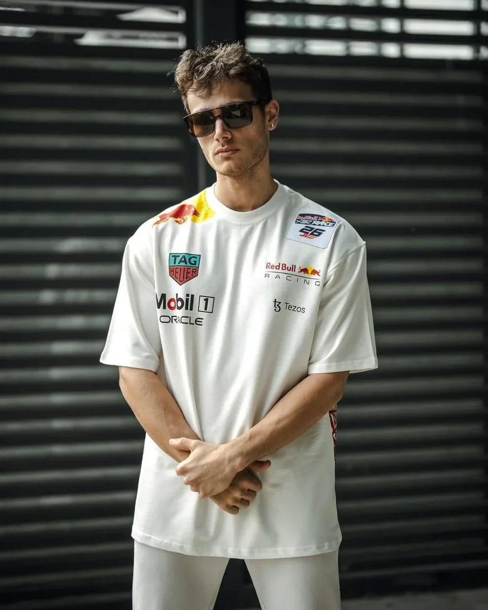 Person wearing a white t-shirt with racing sponsor logos against a metallic background