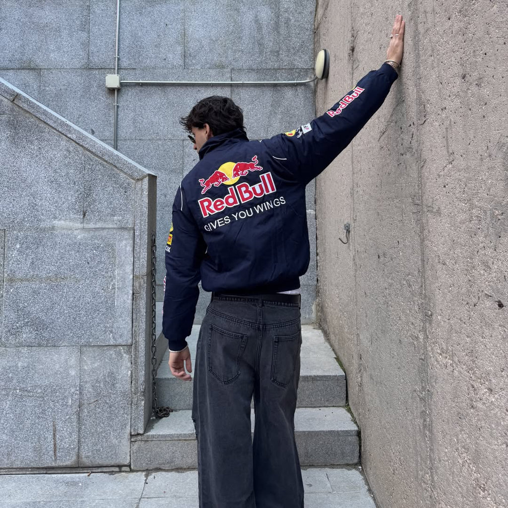 Person wearing a Red Bull jacket leaning against a wall.