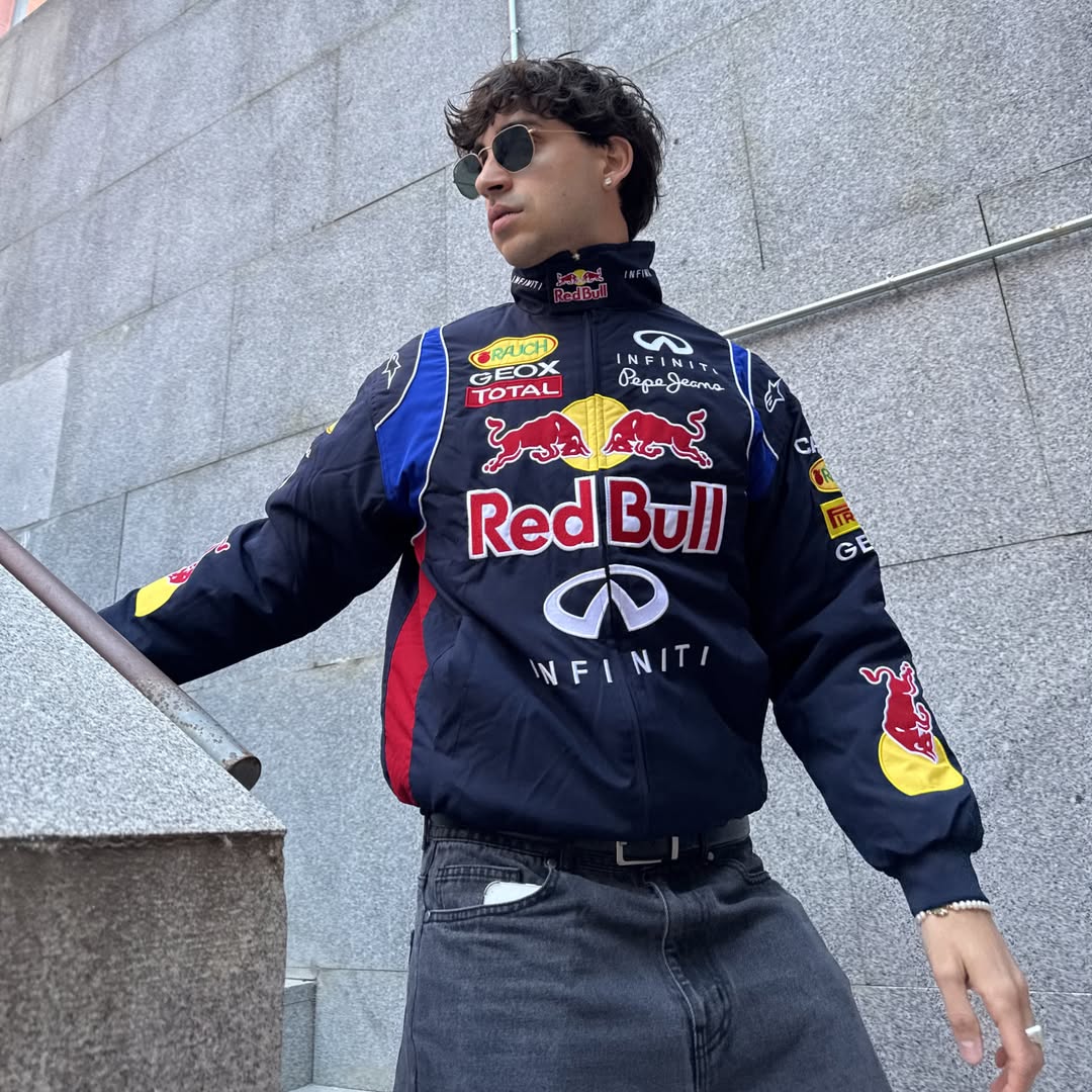 Person wearing a Red Bull racing jacket in front of a gray building.