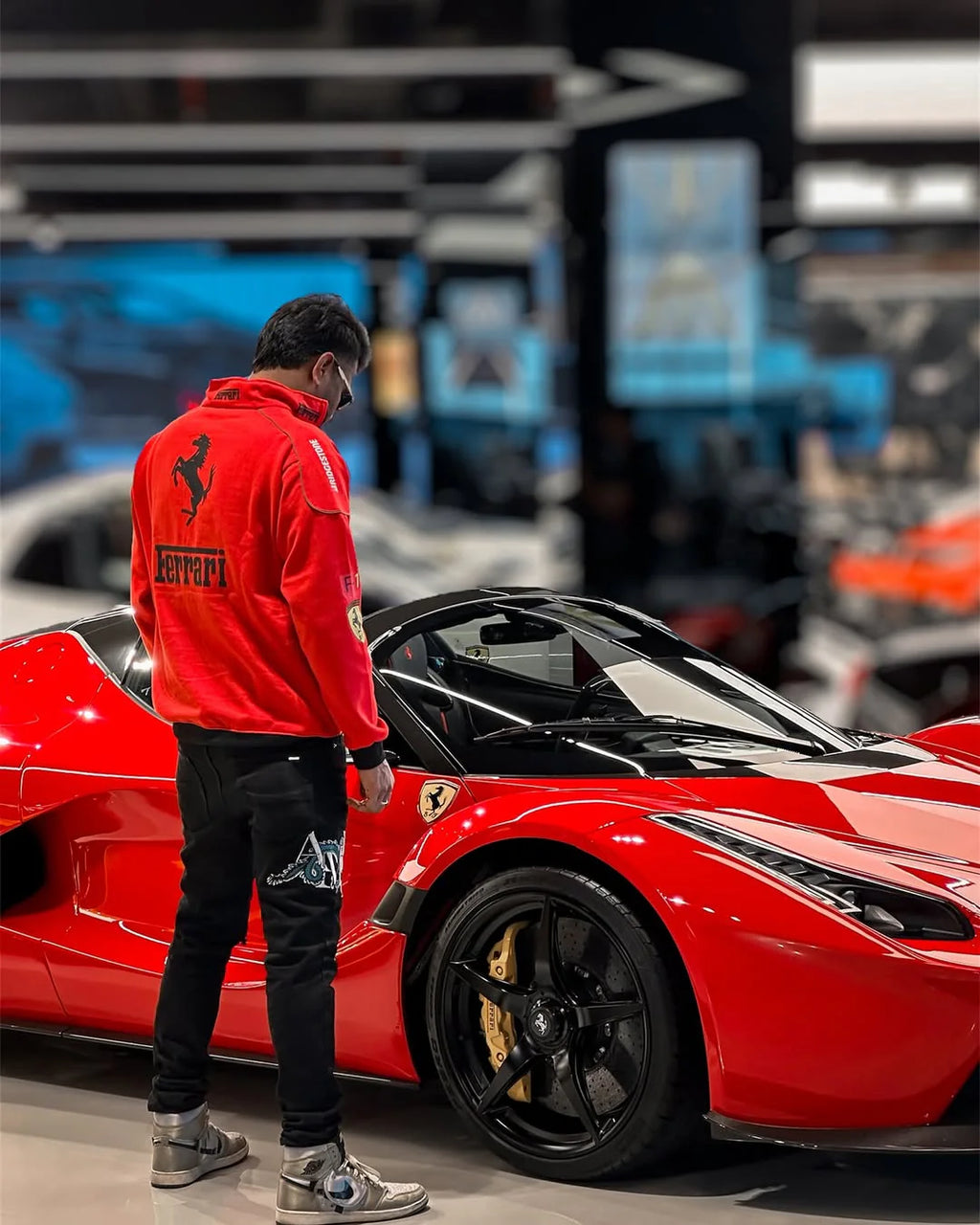 Person wearing a red Ferrari jacket standing next to a red sports car in a showroom.