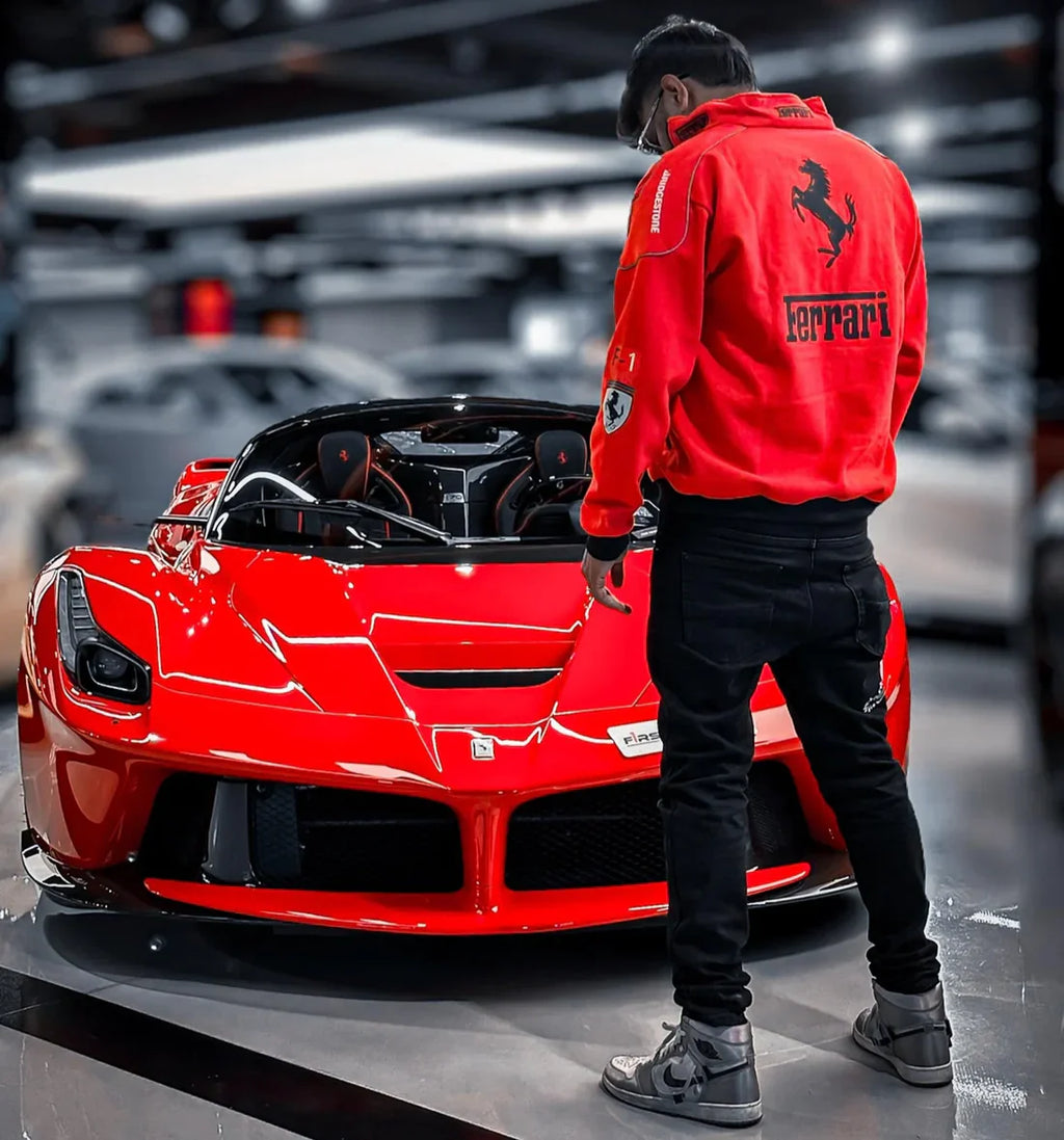 Person wearing a Ferrari jacket standing next to a red Ferrari car in a showroom.