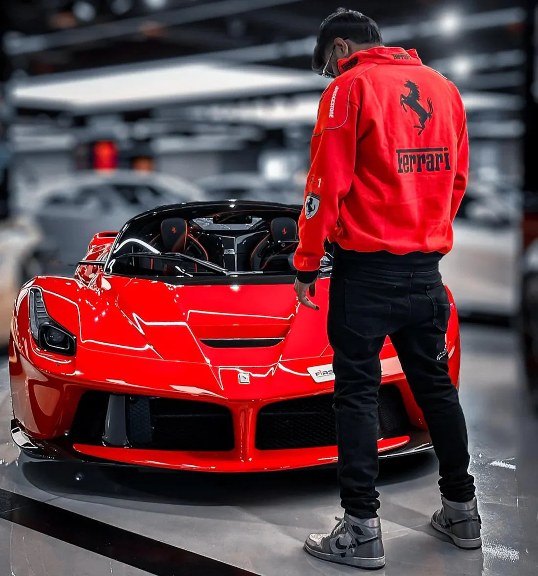 Person wearing a Ferrari jacket standing next to a red Ferrari car in a showroom.