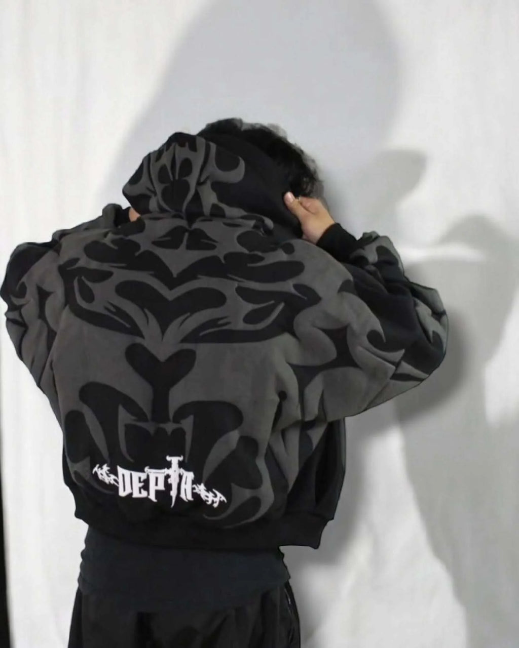 Person wearing a black and gray patterned hoodie with 'Depth' branding on a white background