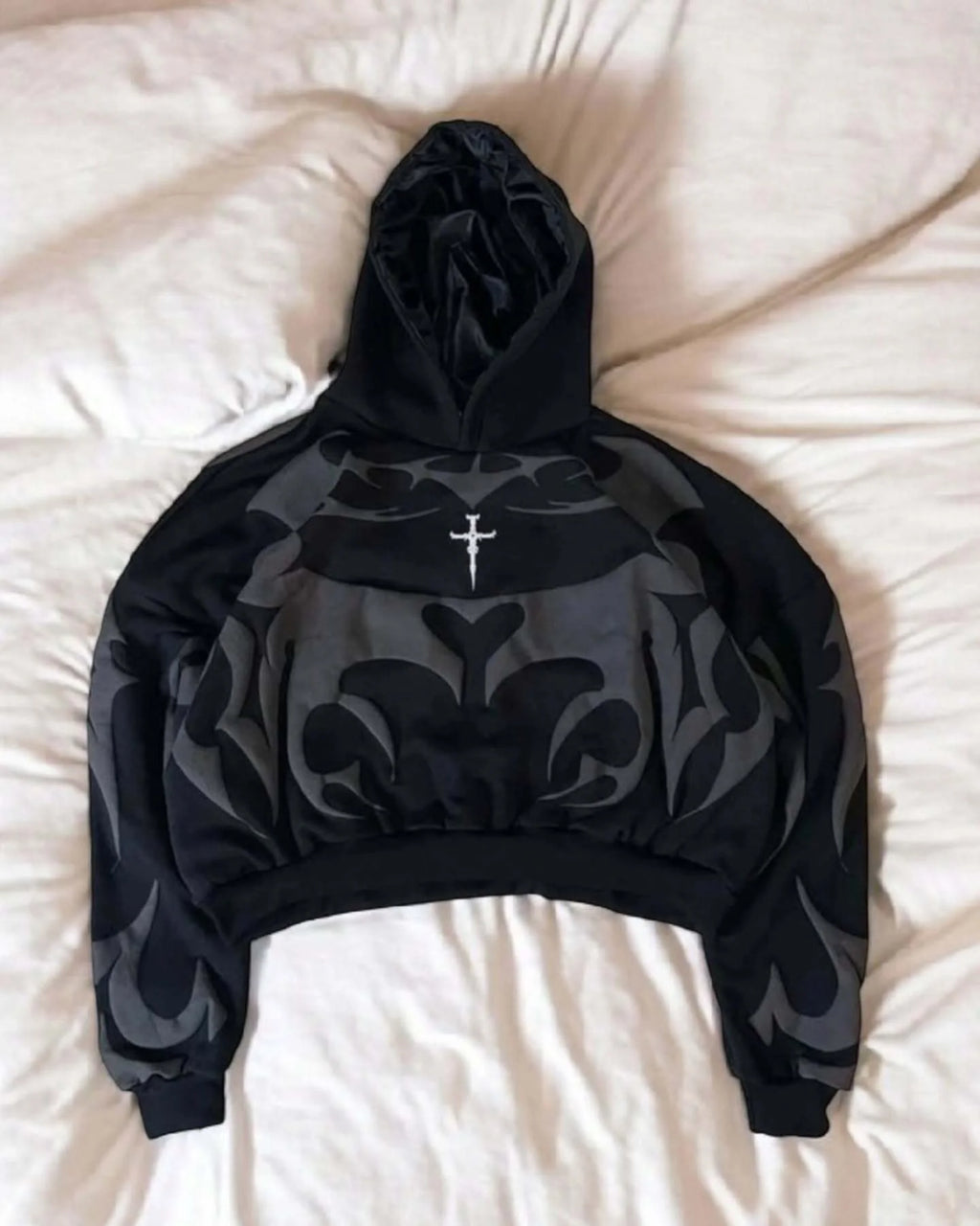 Black hoodie with floral pattern and cross on a white surface